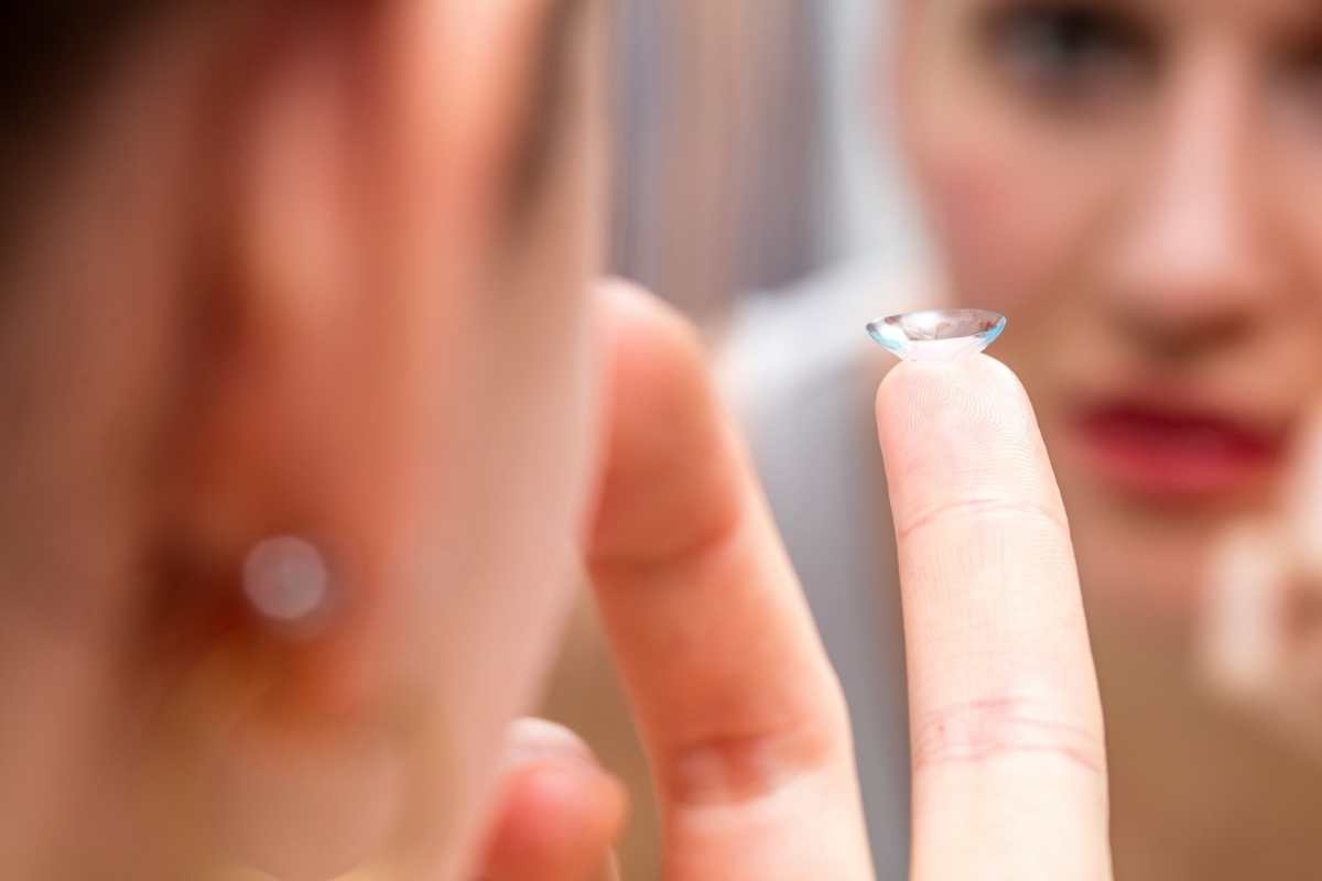 A woman holding up a contact lens in the mirror