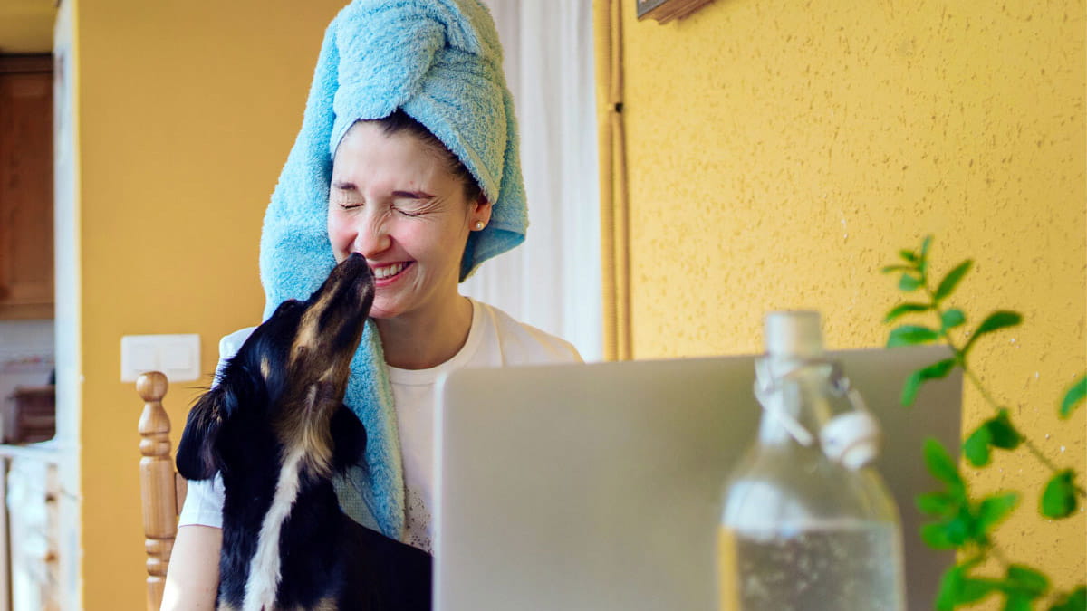 Woman on laptop smiling as dog licks her face