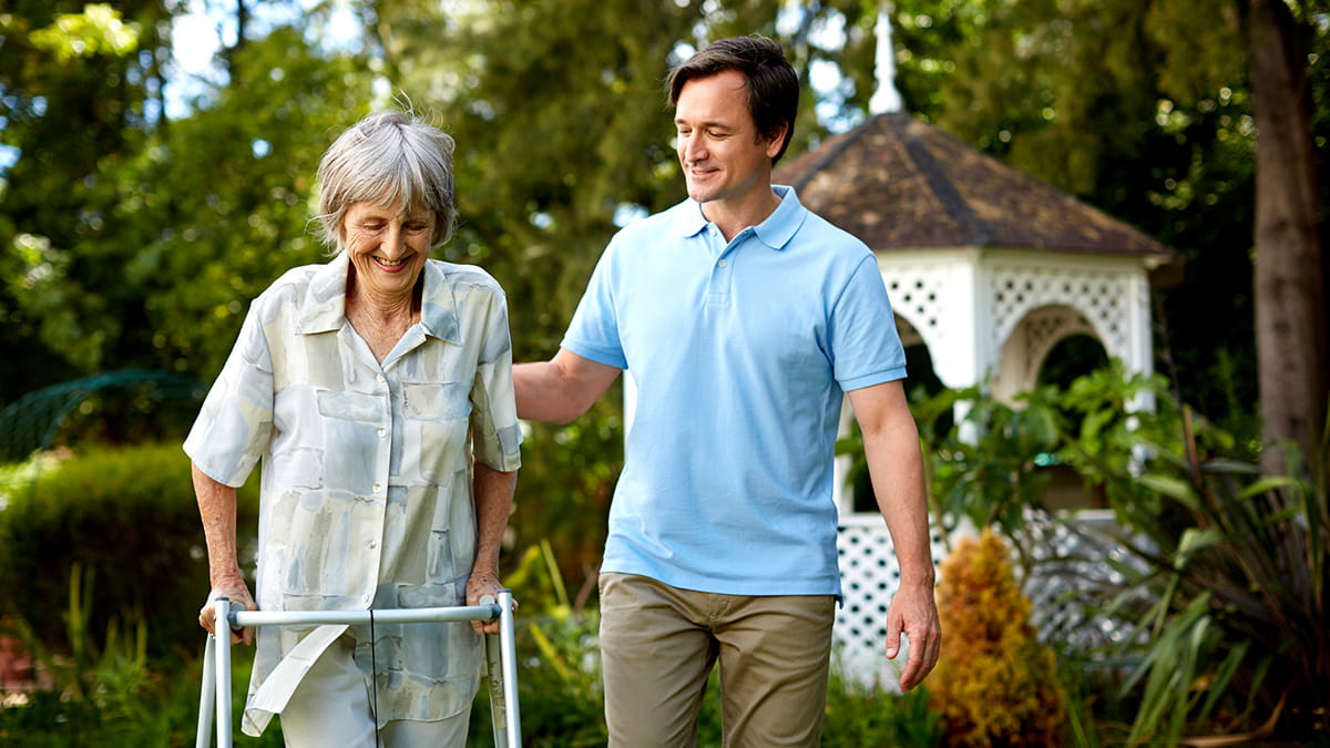 Man assisting an elderly woman with osteoarthritis using her walking aid