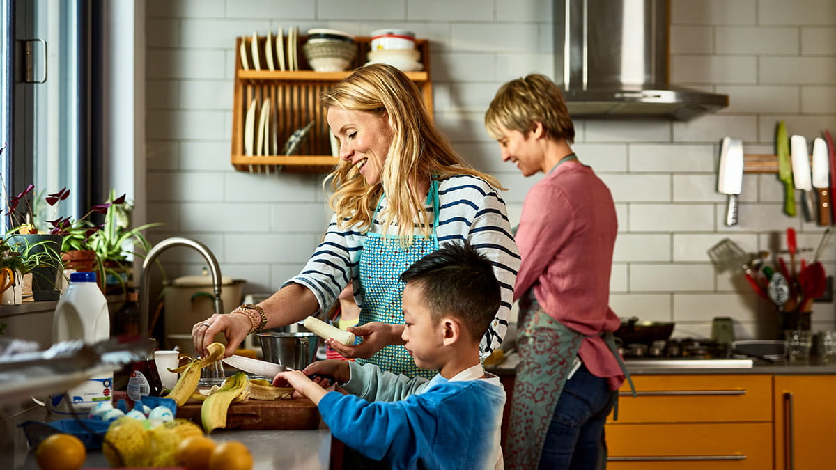 Family preparing food together in a home kitchen, with fruit and ingredients on the bench