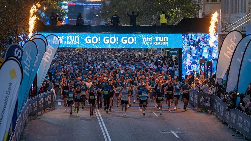 Thousands of participants begin HBF Run for a Reason at the start line in Perth, surrounded by event signage, spectators and pyrotechnic displays.