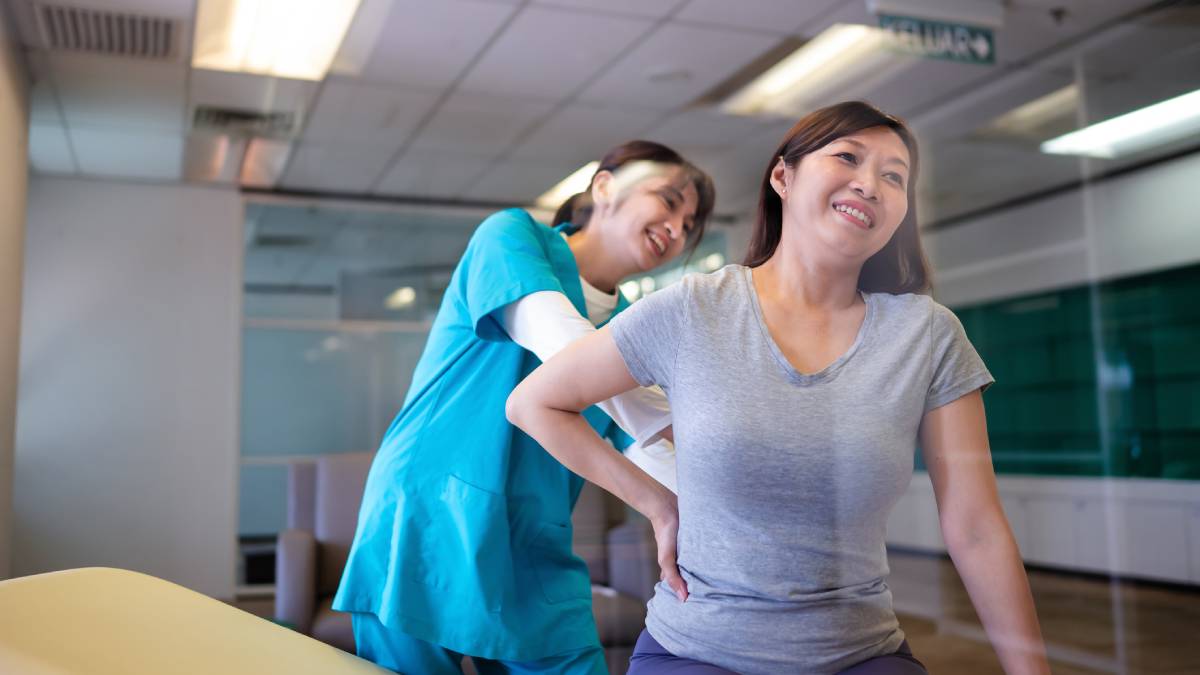 A healthcare professional supports a woman experiencing lower back discomfort during a treatment session