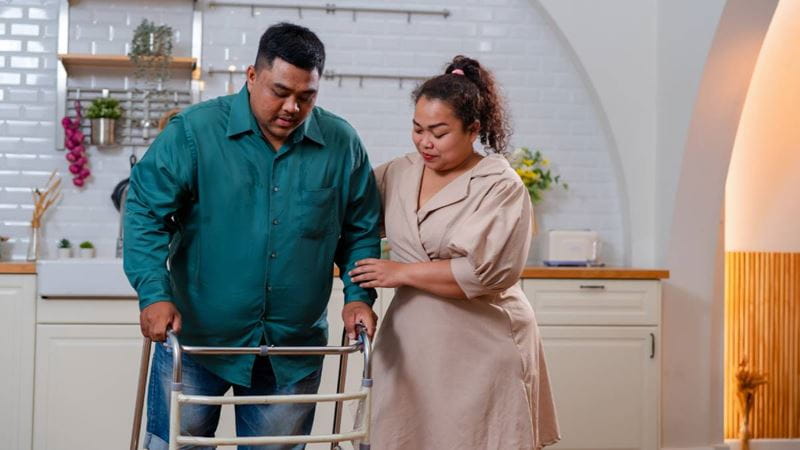 Woman supporting a man using a walking frame following disc replacement surgery