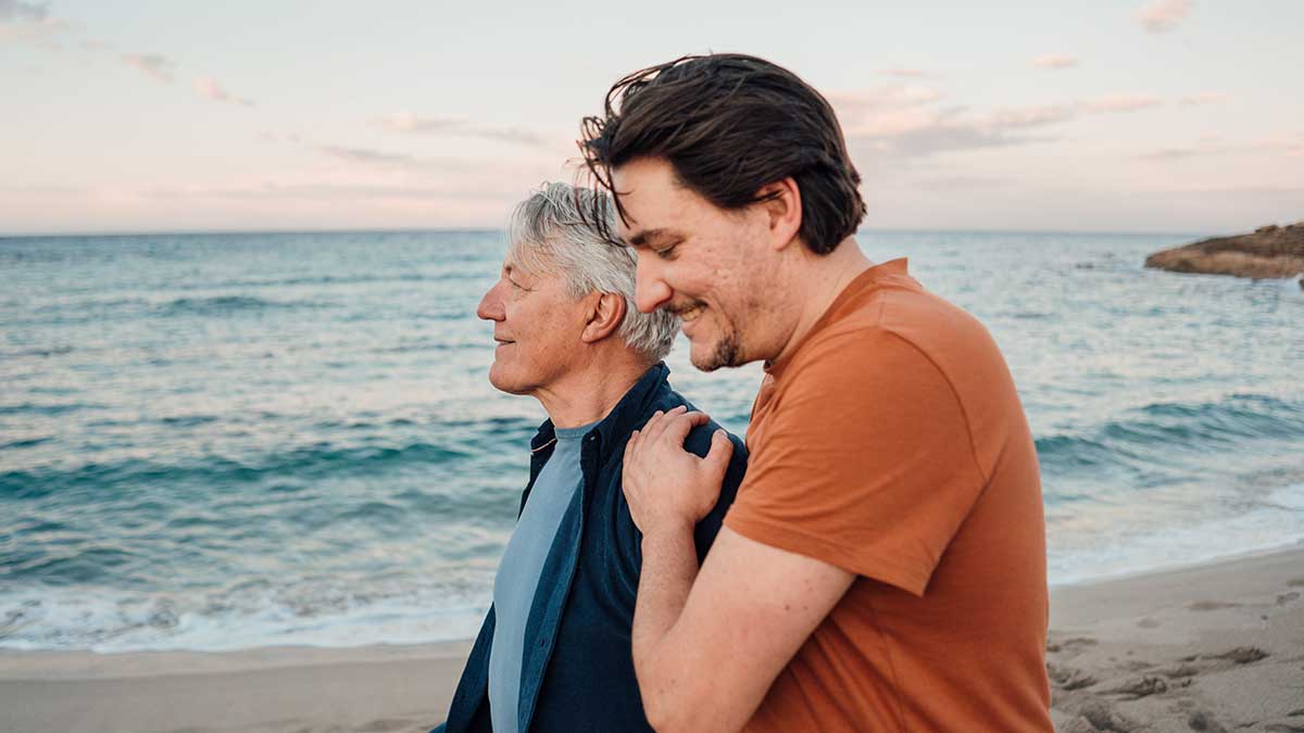 Middle aged man walking along the beach with his elderly father