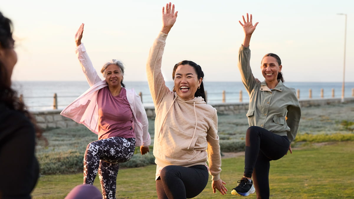 Group of people exercising outdoors near the coast, practising balance and movement as part of a fitness session.