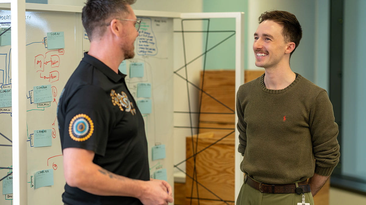 Two employees discussing ideas beside a planning board, highlighting collaboration, communication and career development skills.