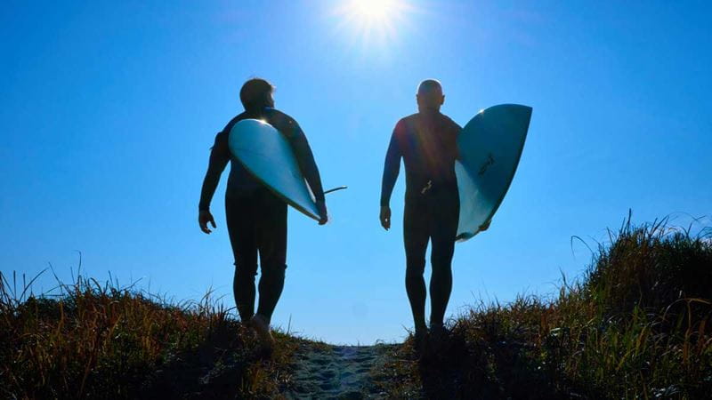 Two men walking to the beach carrying surfboards and wearing wetsuits