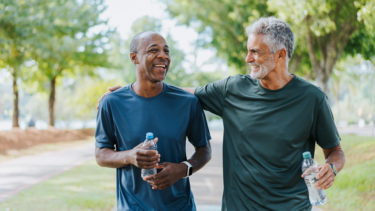Two older men laughing and walking while holding water bottles