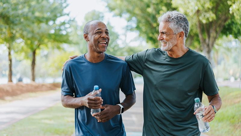 Two older men laughing and walking while holding water bottles