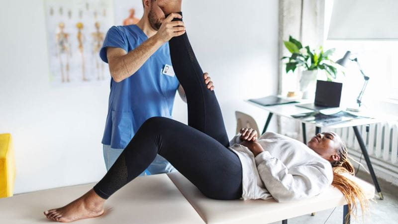 Woman laying on doctors table with leg extended, being treated by physiotherapist