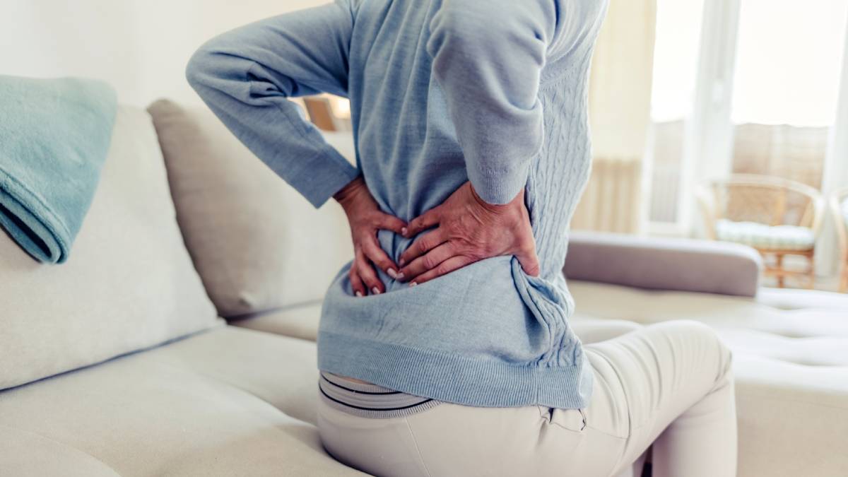 Woman sitting on edge of couch supporting her back with her hands