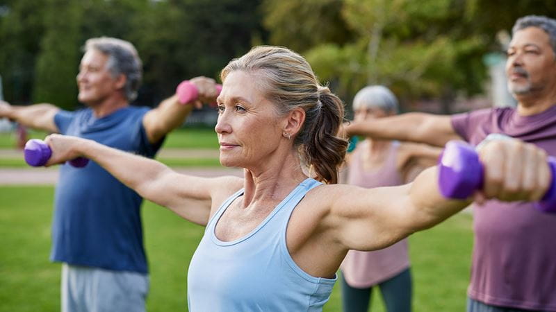 Adults taking part in a resistance training workout with hand weights outdoors to help maintain bone health