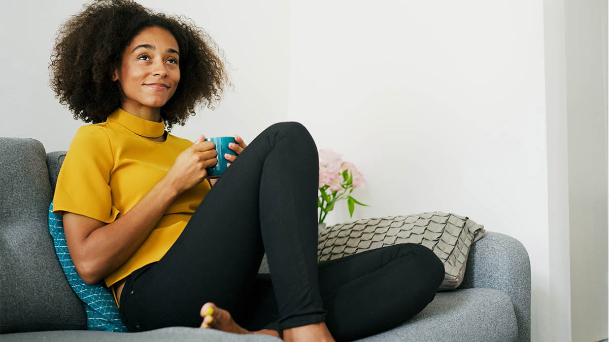 Smiling person with tea relaxing on couch
