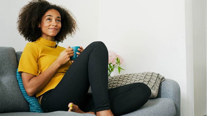 Smiling person with tea relaxing on couch