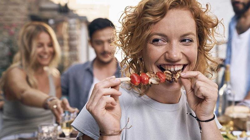 Person smiling while eating a kebab stick