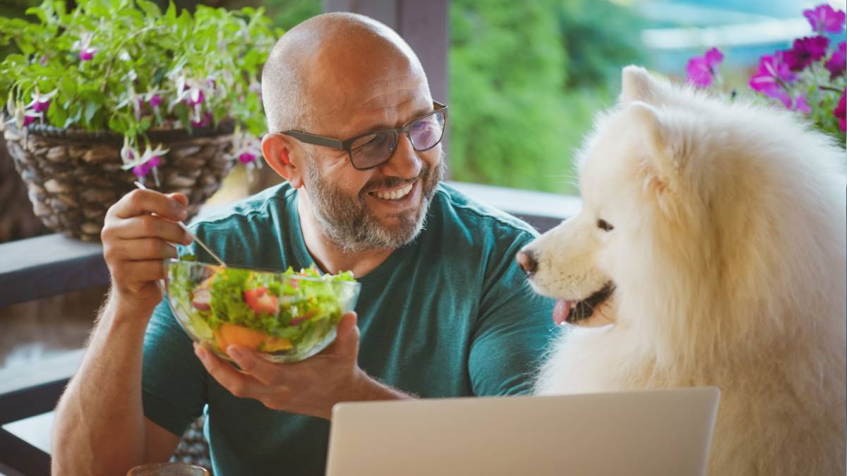 Man eating salad next to dog