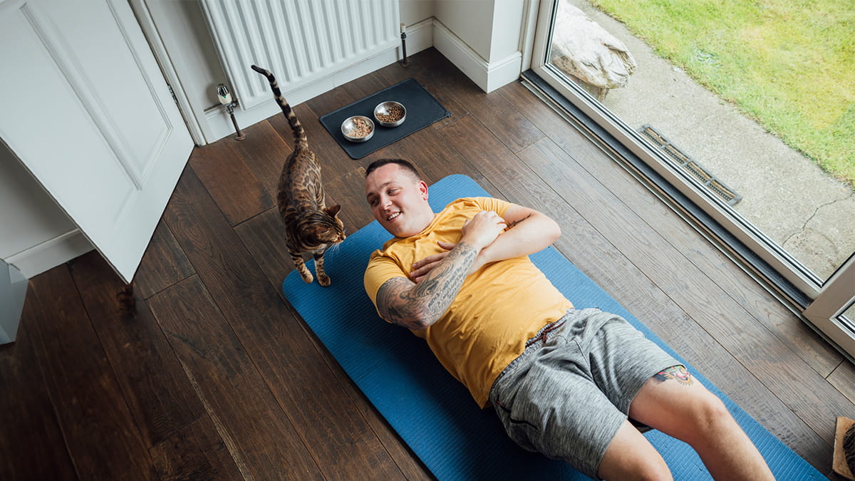 Man stretching with cat standing next to him