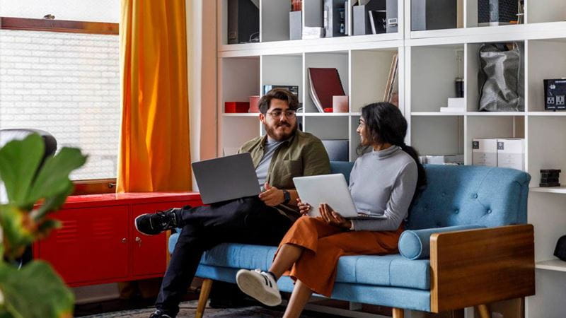 Young couple on couch with laptops looking into percentage back vs set benefits extras