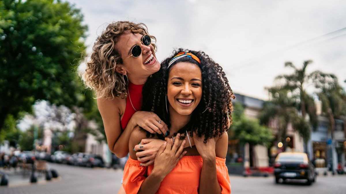Two young woman hugging and having fun on a colourful street