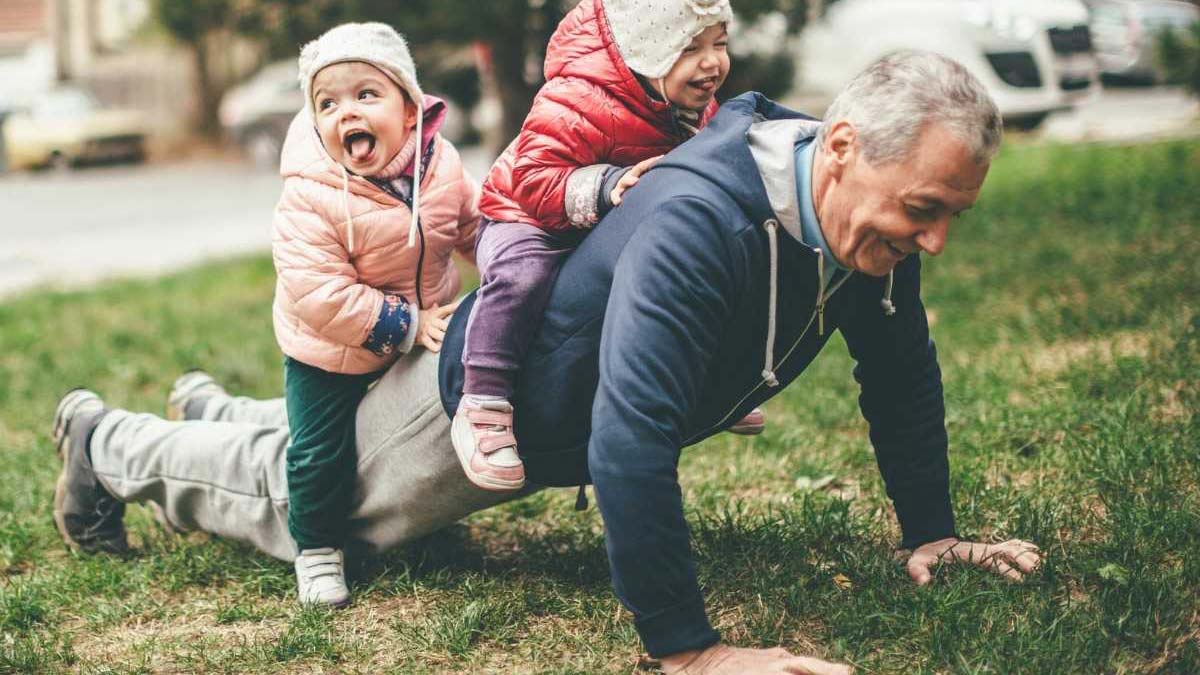 A grandfather doing a push-up with two cute children climbing on his back