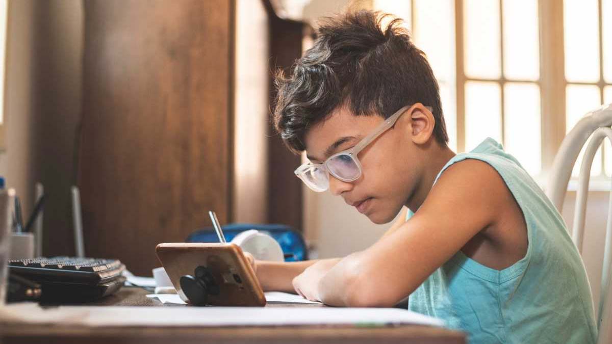 A boy wearing glasses while doing his homework