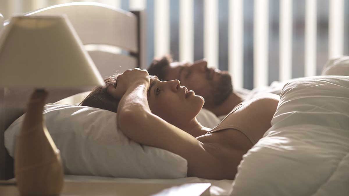 Frustrated woman laying in bed next to sleeping man