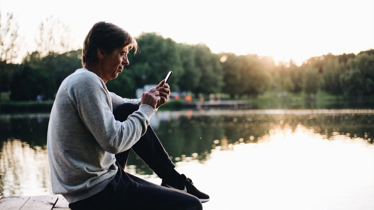 Older man on jetty reading on phone