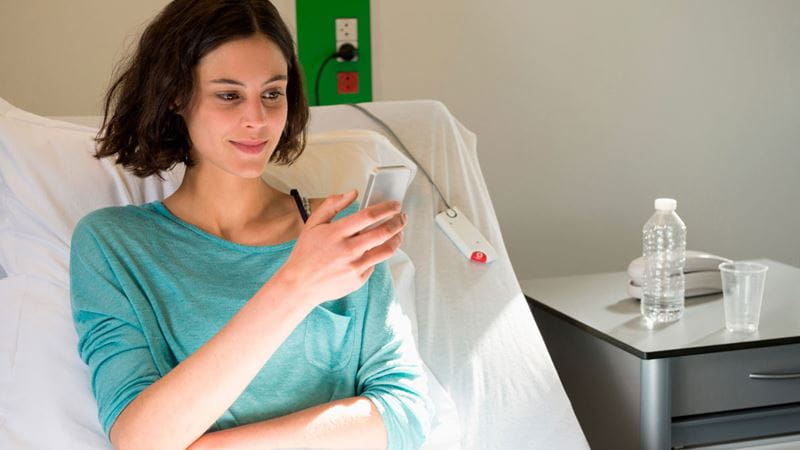 Young woman looking at phone in hospital bed