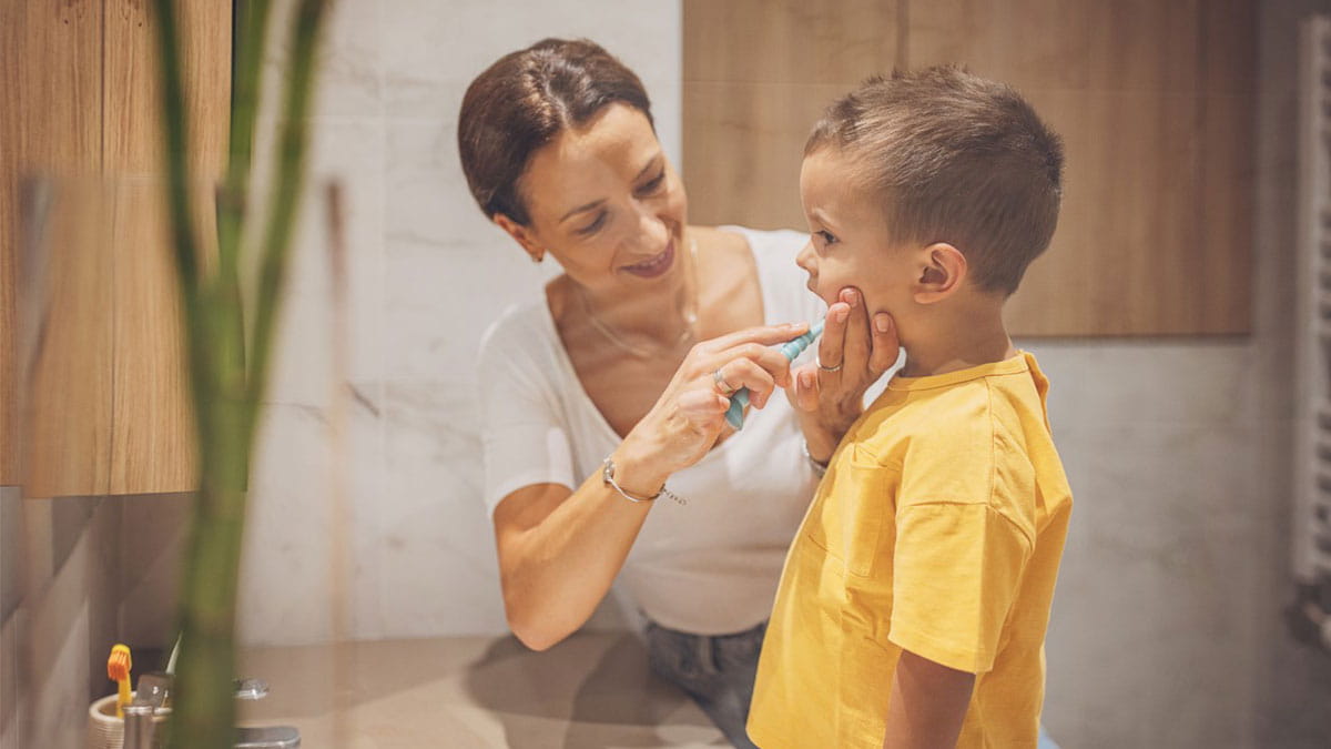 Mother helping son brush teeth