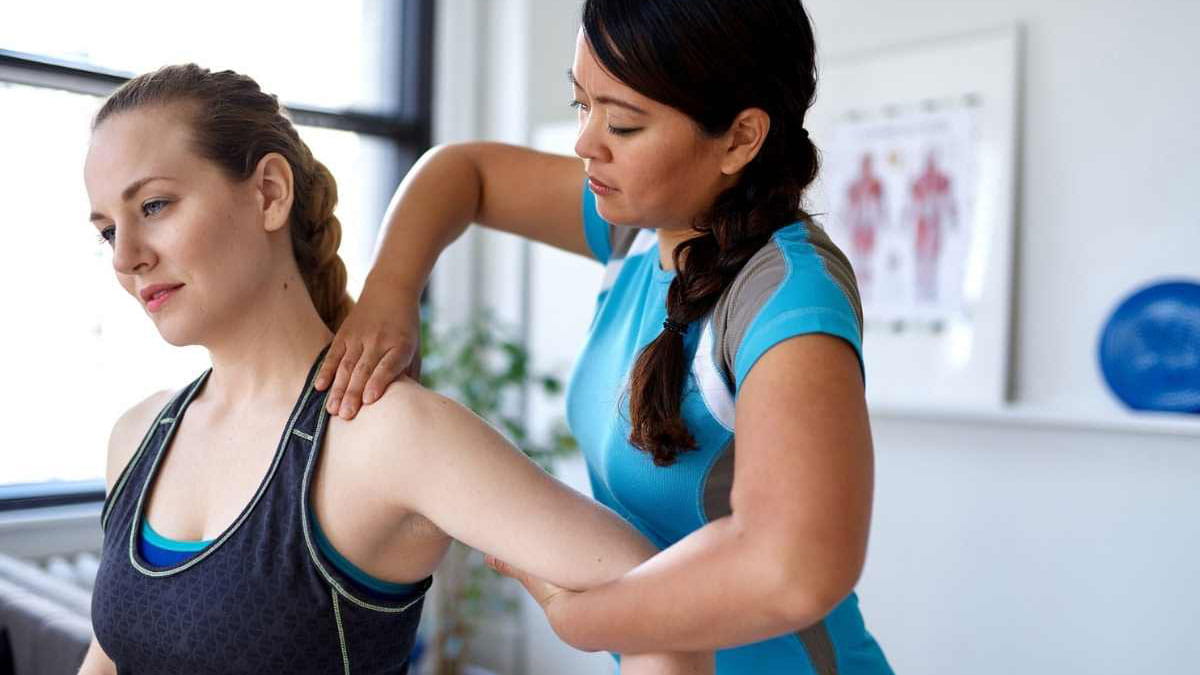 Physiotherapist helping woman stretch her shoulder