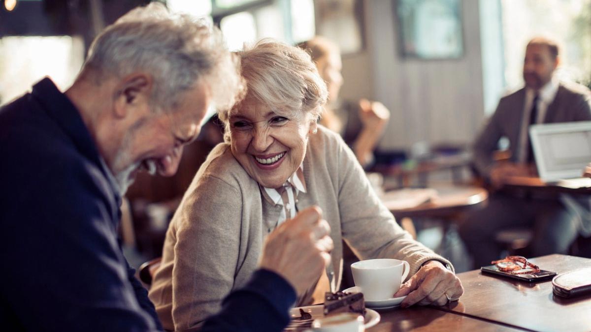 A senior man and woman laughing together in a cafe