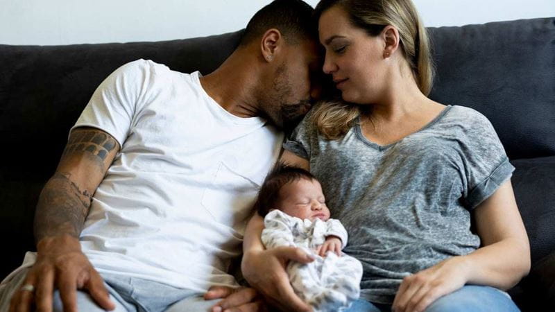 A young couple on the couch holding their newborn baby