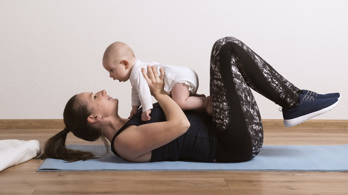 Lady holding her baby while exercising on a yoga mat