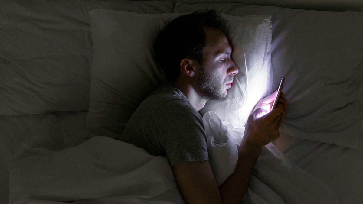 Man laying in bed looking at his phone