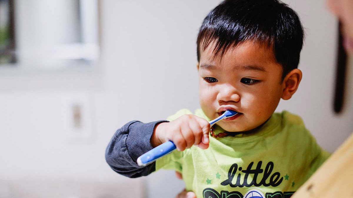 9 month old toddler brushing teeth in mother's arms