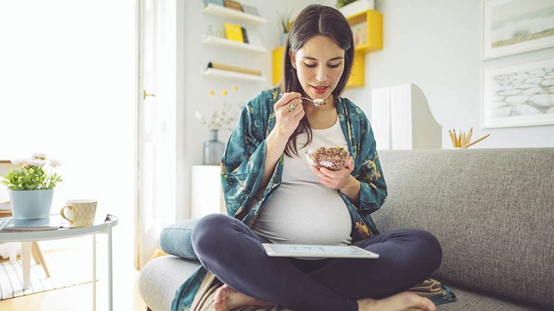 Pregnant woman eating a healthy yogurt while reading her tablet