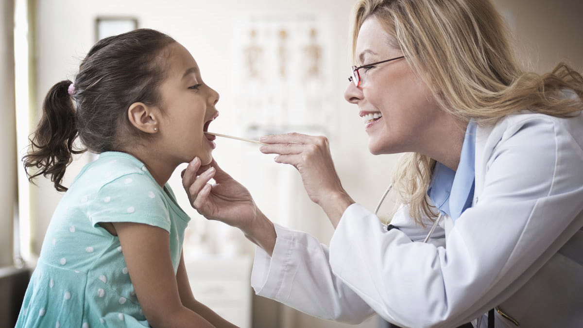 Smiling doctor examining young girls tonsils