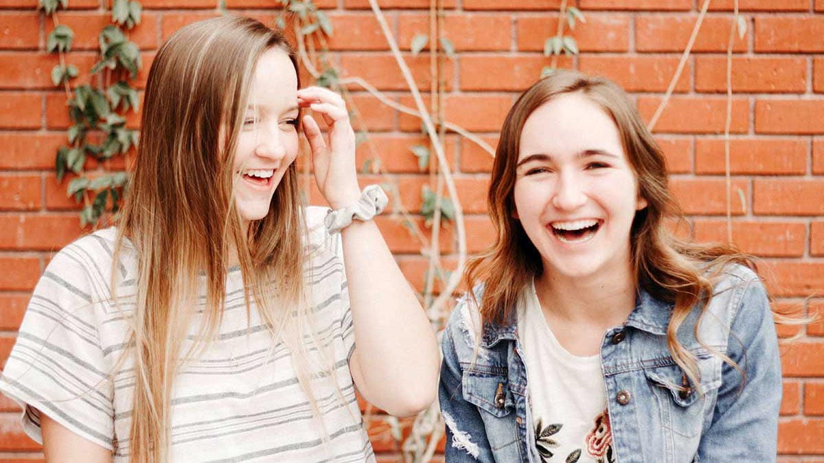 two young women laughing against brick wall background