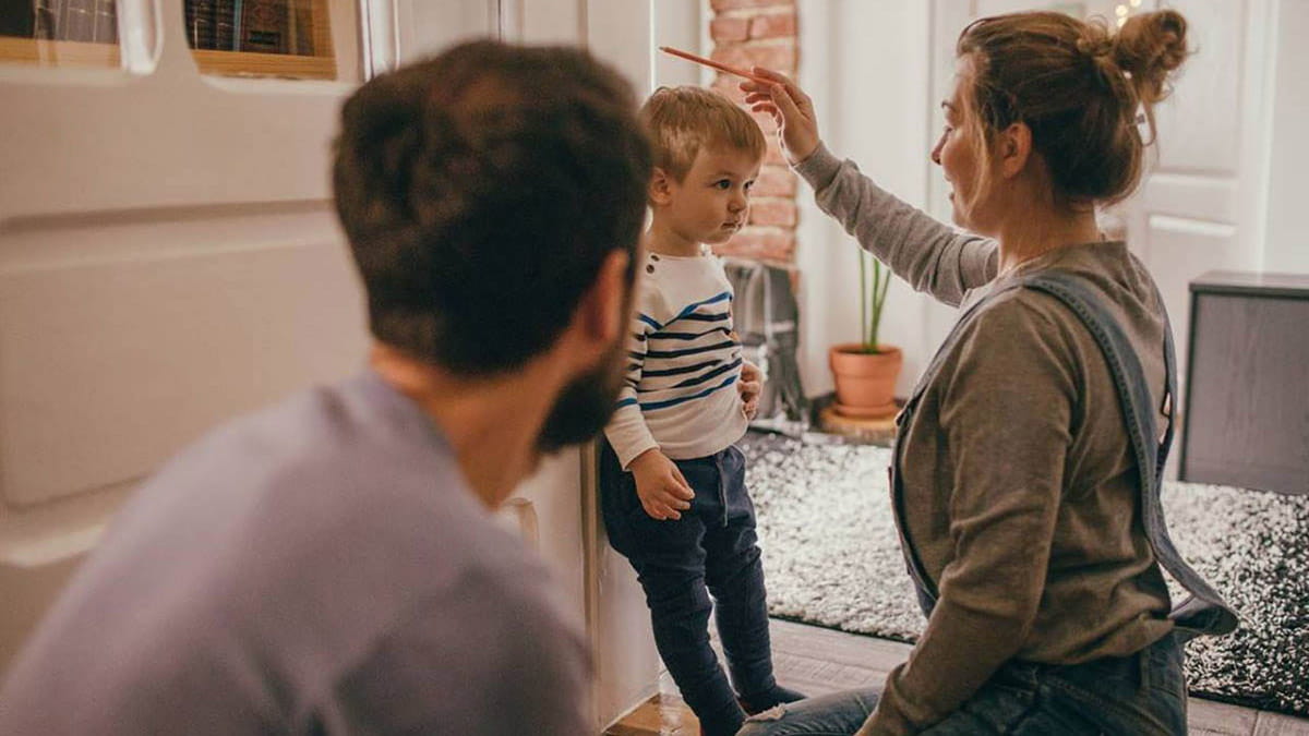 Parents measuring height of growing toddler against wall