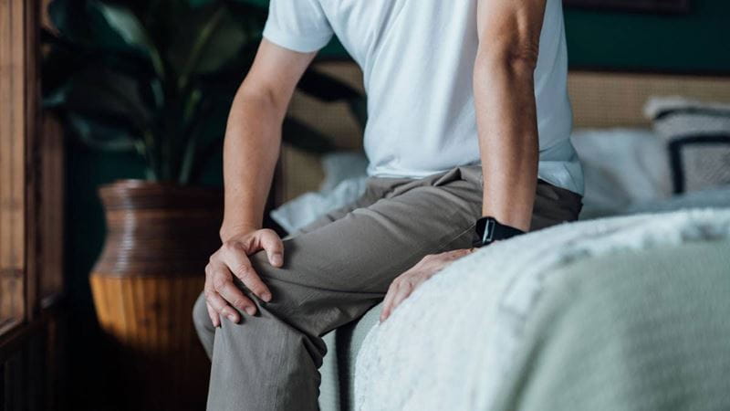 Man sitting on bed holding knee