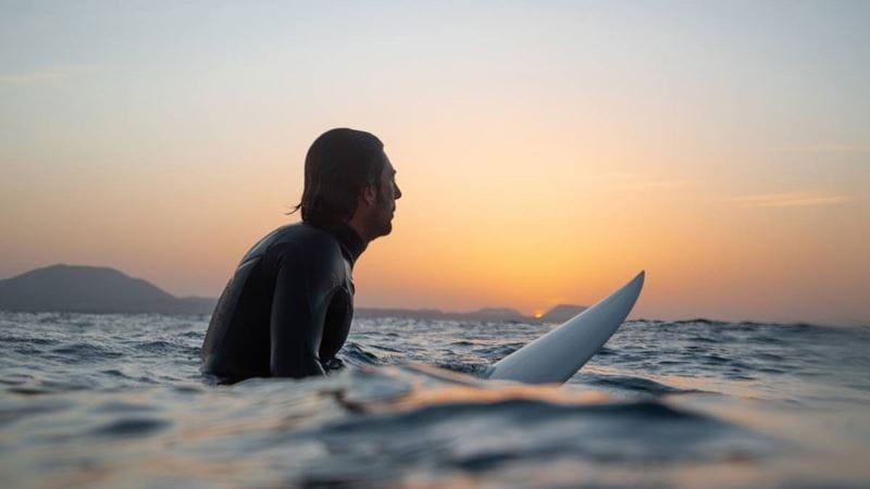 Man sitting on surfboard in middle of the ocean