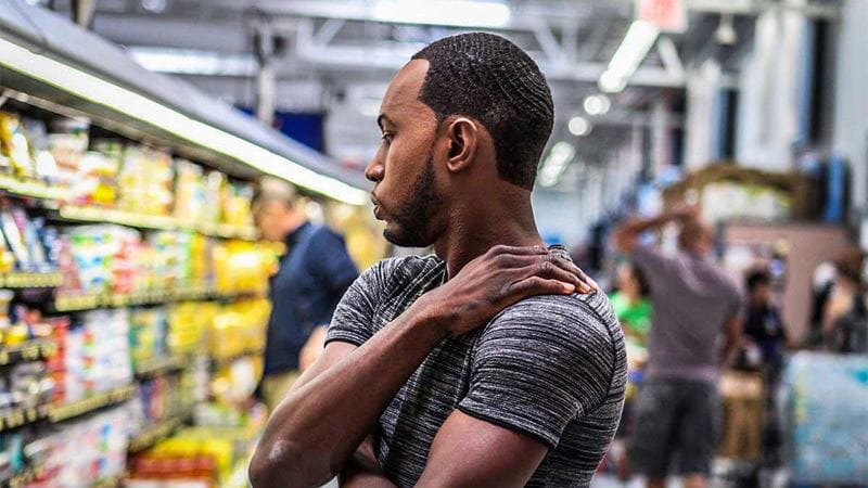 Man in supermarket rubbing painful shoulder