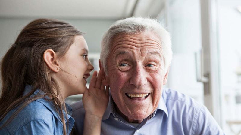 Young girl speaking into grandfather's ear