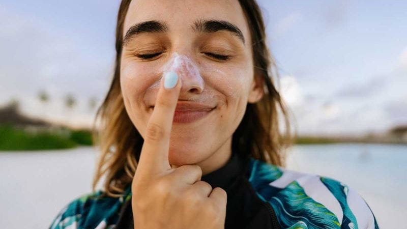 A young woman at the beach put sunscreen on her nose and smiling