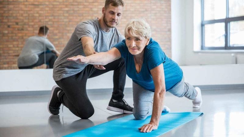 A physiotherapist helping a mature woman with strength and mobility exercises