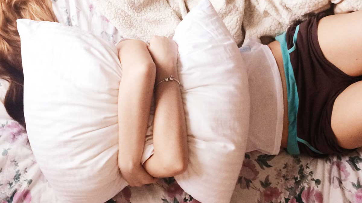 Frustrated young woman clutching pillow over face on bed