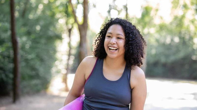 A happy woman outside with a yoga mat