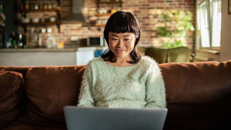 Woman on the couch submiting her claim to HBF on a laptop