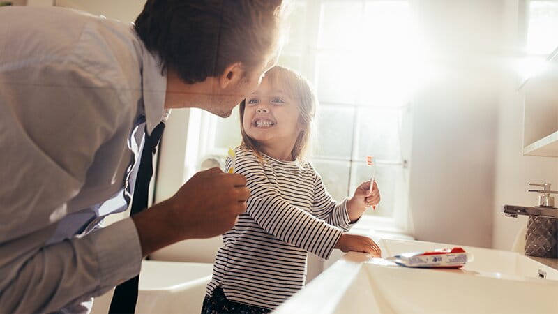 Young daughter and father brushing teeth together in the bathroom
