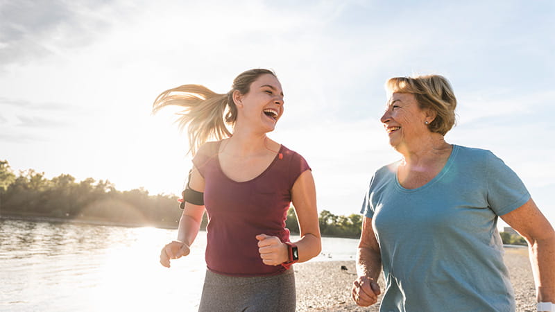 Mother and daughter running along the beach together while laughing